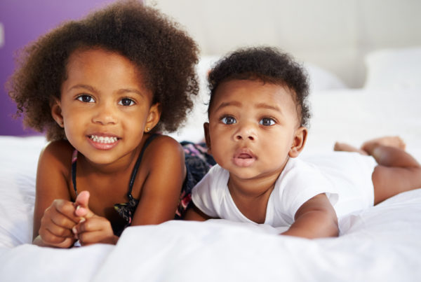 Sister With Baby Brother Lying On Parent's Bed